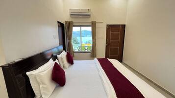 A hotel room with a bed, a window with curtains, an air conditioning unit, and a door.