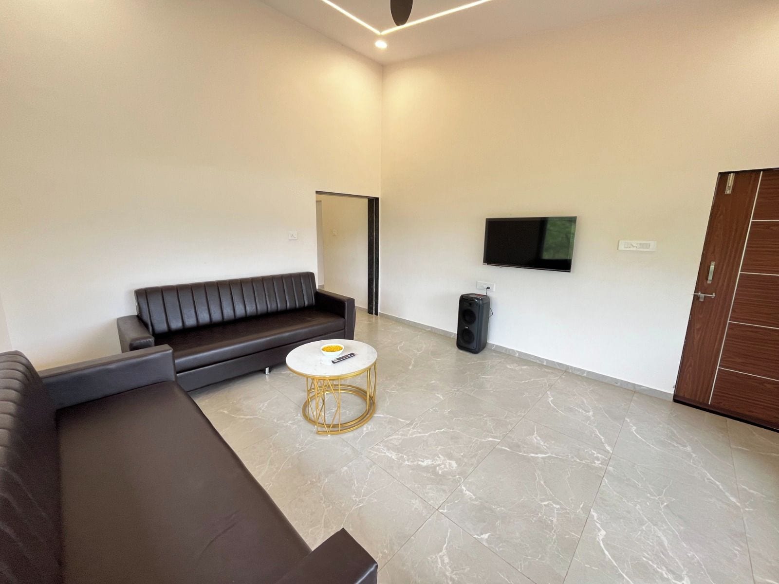 A modern living room with a dark leather sofa, a round coffee table, and a flat-screen TV mounted on the wall.