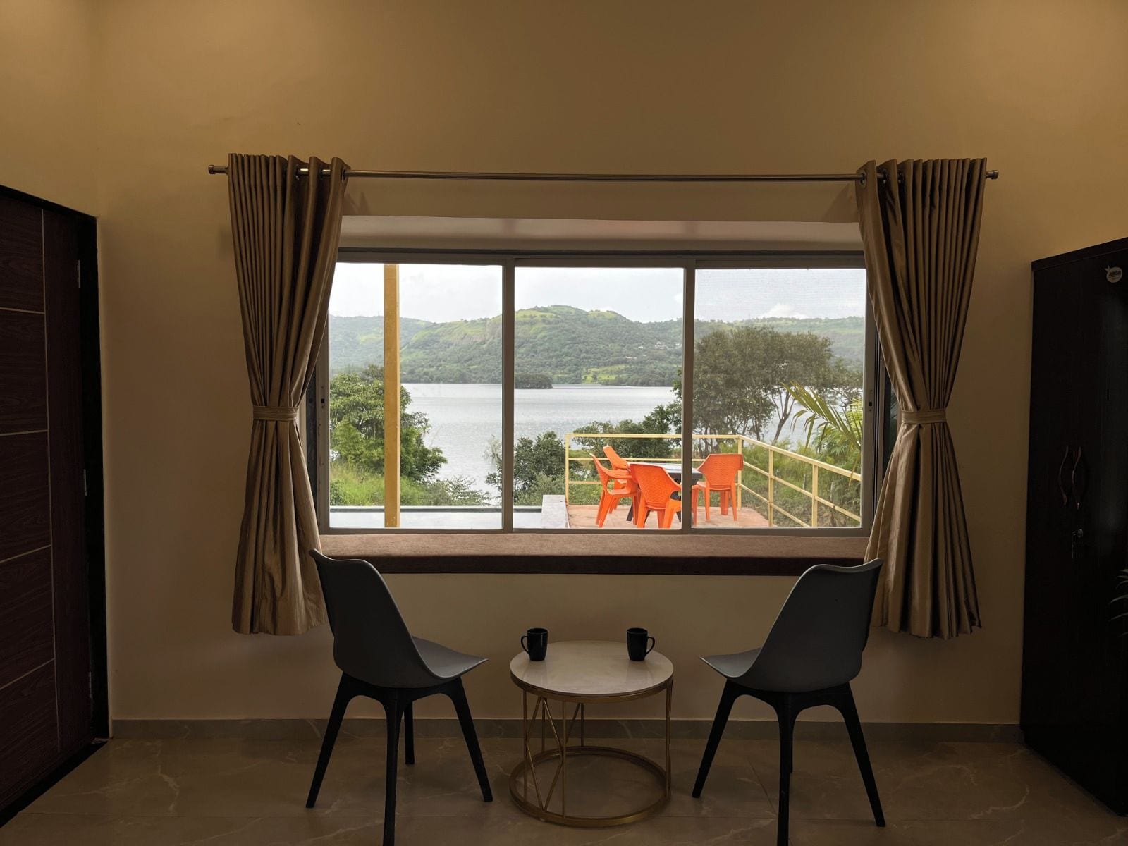 Une pièce dotée d’une grande fenêtre donnant sur un lac, de deux fauteuils et d’une petite table.