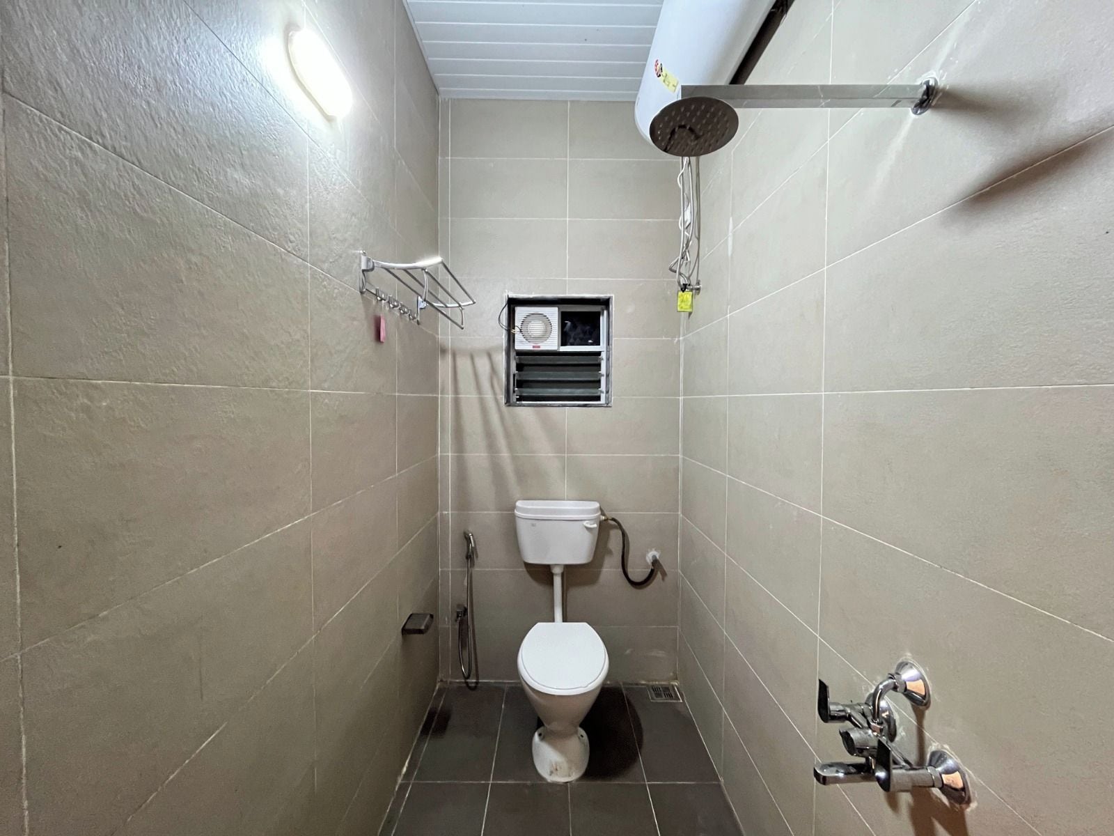 Une petite salle de bain carrelée, équipée de toilettes, d’une douche et d’un porte-serviettes.