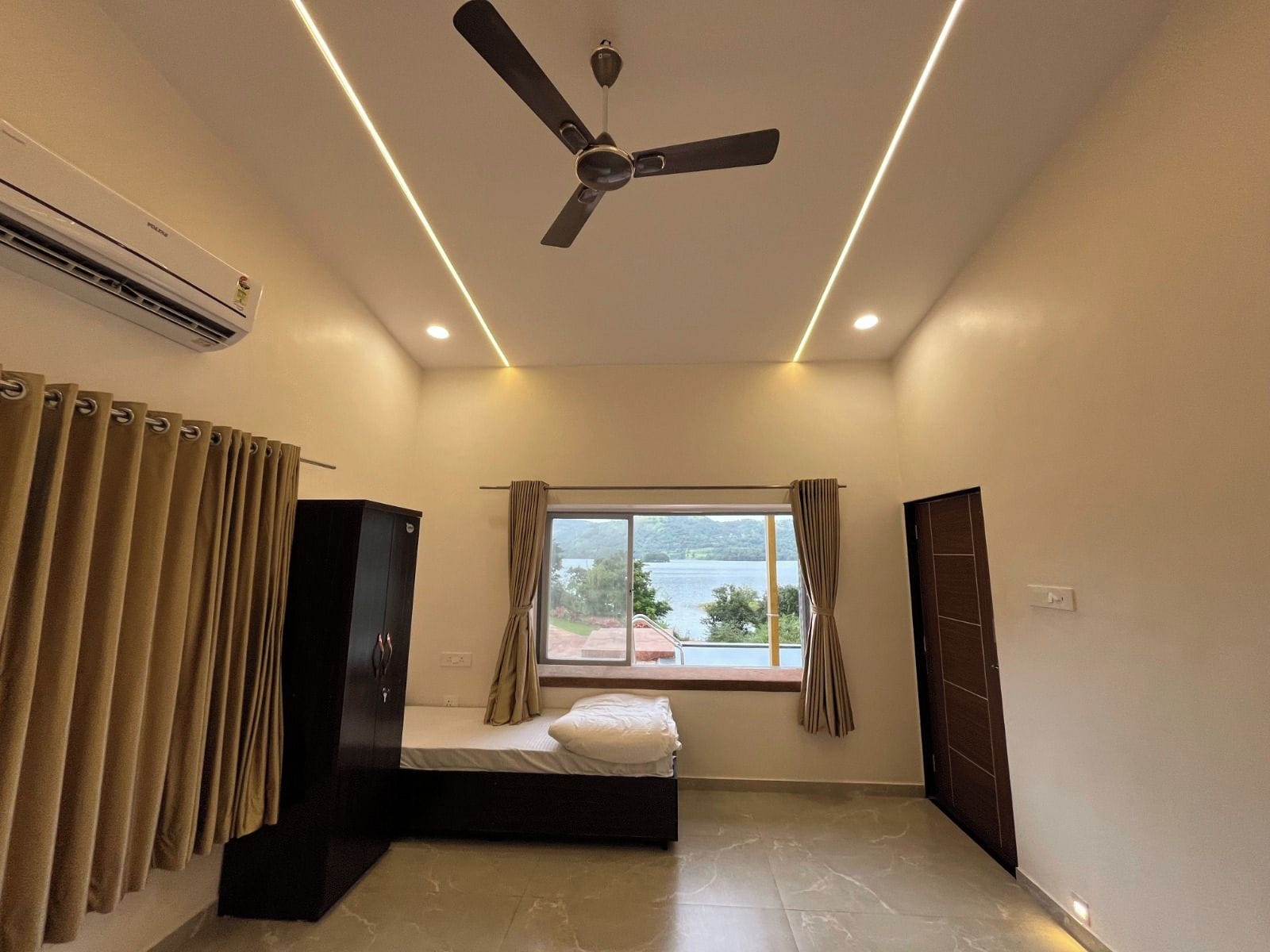 Una camera da letto con un letto, una ventola a soffitto, un condizionatore d'aria, una finestra con tende e vista su un corpo d'acqua.