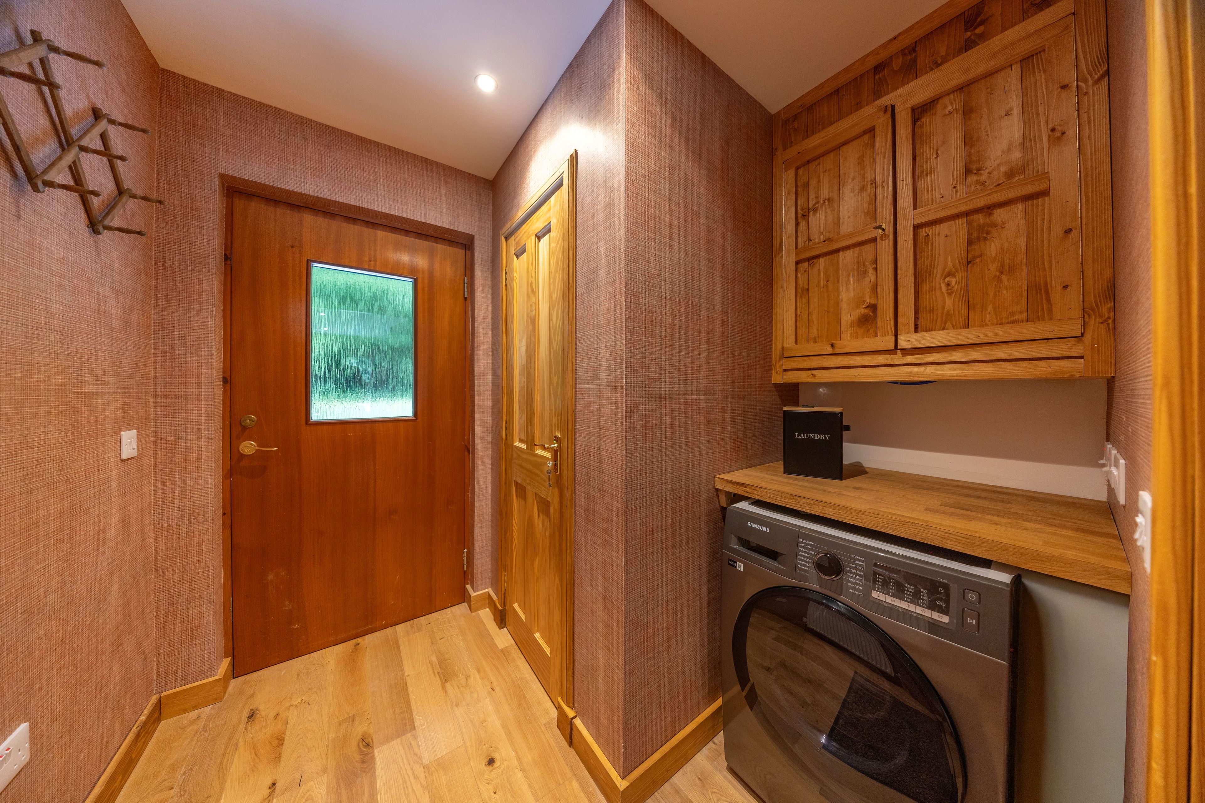 A laundry area with a washing machine, wooden cabinets, and a door with a window.