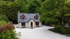 A house with a symmetrical facade, a central entrance, and a gravel driveway. - The Log Cabin at Rokeby Manor (Invergarry)