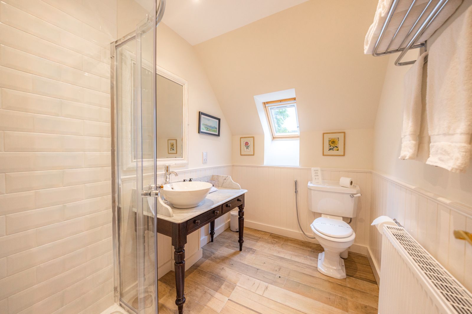 A bathroom with a glass shower enclosure, a white sink, a toilet, and a window providing natural light.