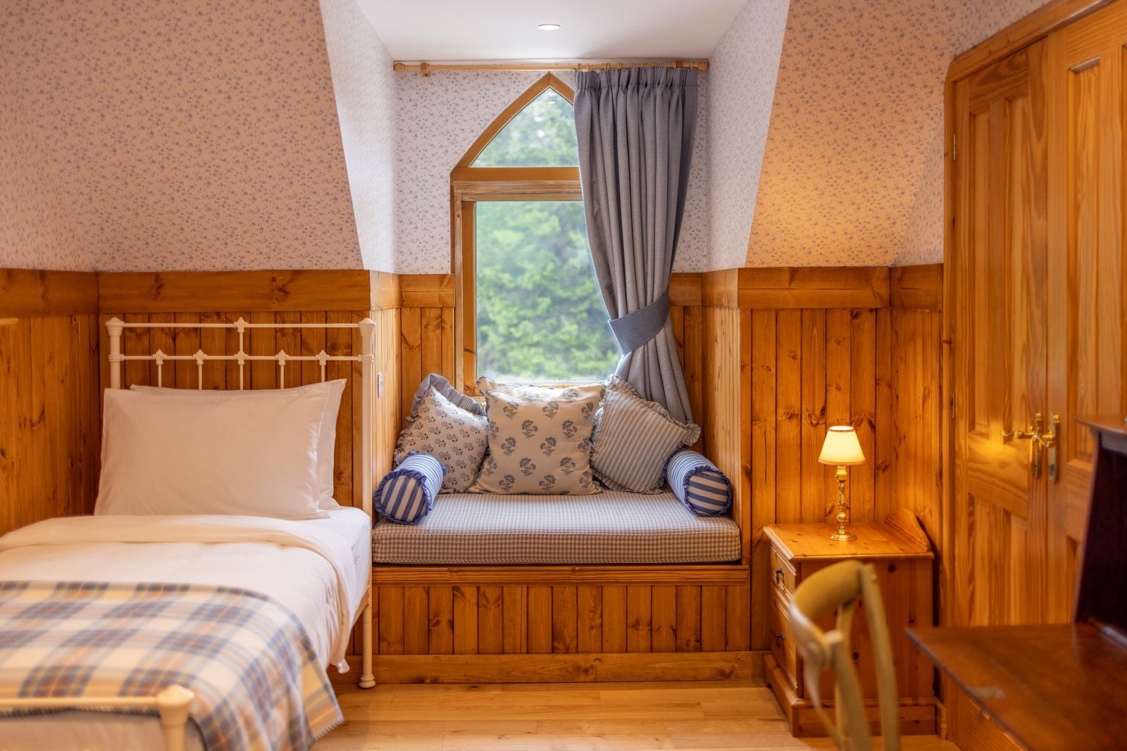 Ein gemütliches Zimmer mit einem Bett, einer Bank mit Kissen, einem kleinen Tisch mit einer Lampe und Holzwänden.