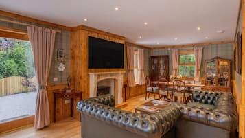 Un salon avec une cheminée, des canapés en cuir, un téléviseur et un coin repas.