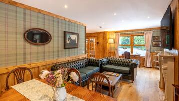Ein gemütliches Zimmer mit Holzboden, einem grünen Sofa, einem Esstisch mit Stühlen und einem Blumenstrauß.