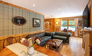 A cozy room with a wooden floor, a green sofa, a dining table with chairs, and a vase of flowers. - The Log Cabin at Rokeby Manor (Invergarry)