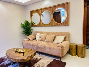 Una sala de estar con un sofá, una mesa de centro, una mesita auxiliar de madera, un espejo y una planta.