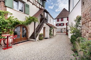 A narrow cobblestone alley with buildings on either side, a staircase leading to a second floor, and a red table with chairs outside a door. - Apartment 'Lucia - Duplex Climatisé' with Mountain View, Wi-Fi and Air Conditioning (Obernai)