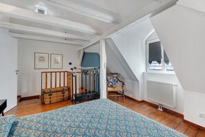 A bedroom with a bed, a wooden chest, a window with blinds, and a chair with a cushion. - Apartment 'Lucia - Duplex Climatisé' with Mountain View, Wi-Fi and Air Conditioning (Obernai)