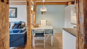 Una habitación acogedora con techo de madera, una mesa de comedor con mantel floral, un sofá azul y una silla blanca.