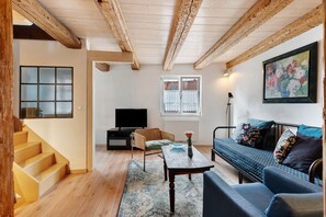 Een woonkamer met een bank, een televisie, een salontafel en een trap.