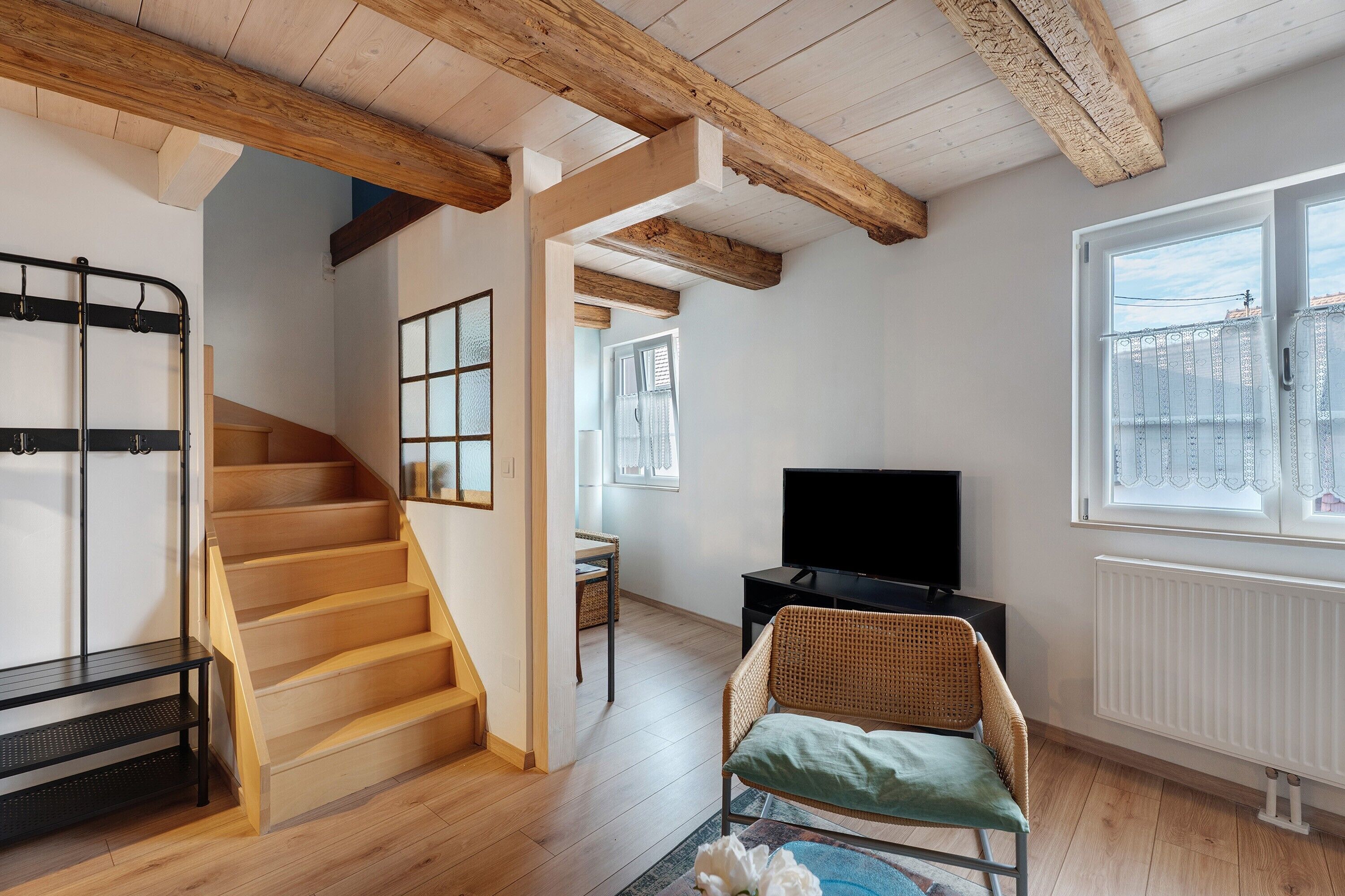 Un interno moderno con una scala in legno, una televisione e una poltrona in vimini.