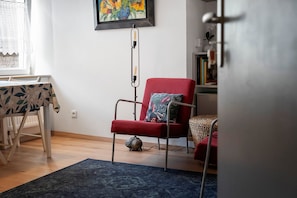 A room with a red chair, a table with a floral tablecloth, a blue rug, and a painting on the wall. - Studio "Casa Lucia - Air Conditioning" with Wi-Fi and Air Conditioning (Obernai)