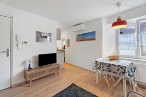 A modern living room with a TV, wooden entertainment unit, and a dining area with a table and chairs. - Studio "Casa Lucia - Air Conditioning" with Wi-Fi and Air Conditioning (Obernai)