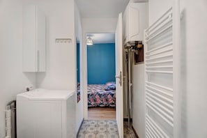 A narrow hallway with a bed in the background, a white radiator, and a washing machine. - Studio "Casa Lucia - Air Conditioning" with Wi-Fi and Air Conditioning (Obernai)