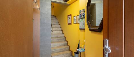 Un pasillo con una escalera, una puerta de madera, un espejo y una pared decorada con cuadros.