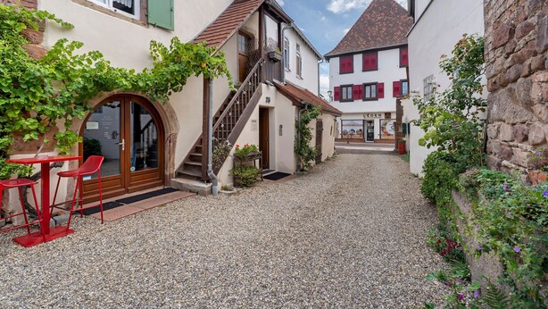 Un patio con un sendero de grava, una escalera y un edificio con una puerta y ventanas.