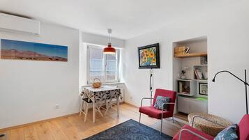 Een moderne woonkamer met een eethoek, een rode fauteuil, een boekenkast en een schilderij aan de muur.