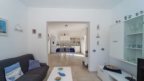 Ein modernes Wohnzimmer mit einem dunkelgrauen Sofa, einem weißen Couchtisch mit dekorativen, fischförmigen Schalen und einer Vitrine mit Geschirr.
