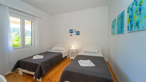 A room with two beds, a window with curtains, a bedside table with a lamp, and wall art.
