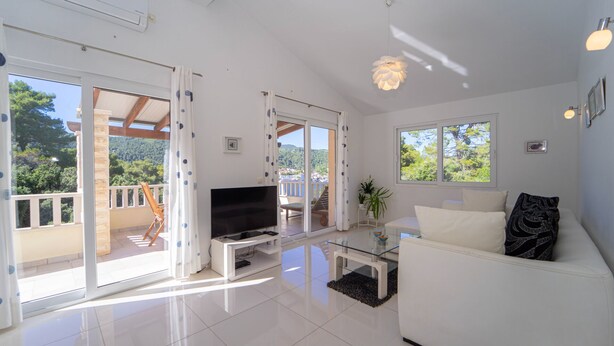 A modern living room with a flat-screen TV, a glass coffee table, and a white sofa.