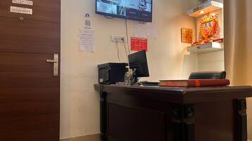 A reception desk with a flat-screen TV, a computer, and a telephone. There are signs for reception and hotel information, including a QR code.