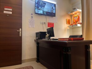 A reception desk with a flat-screen TV, a computer, and a telephone. There are signs for reception and hotel information, including a QR code. - Smart Stay Malviya Nagar (New Delhi)