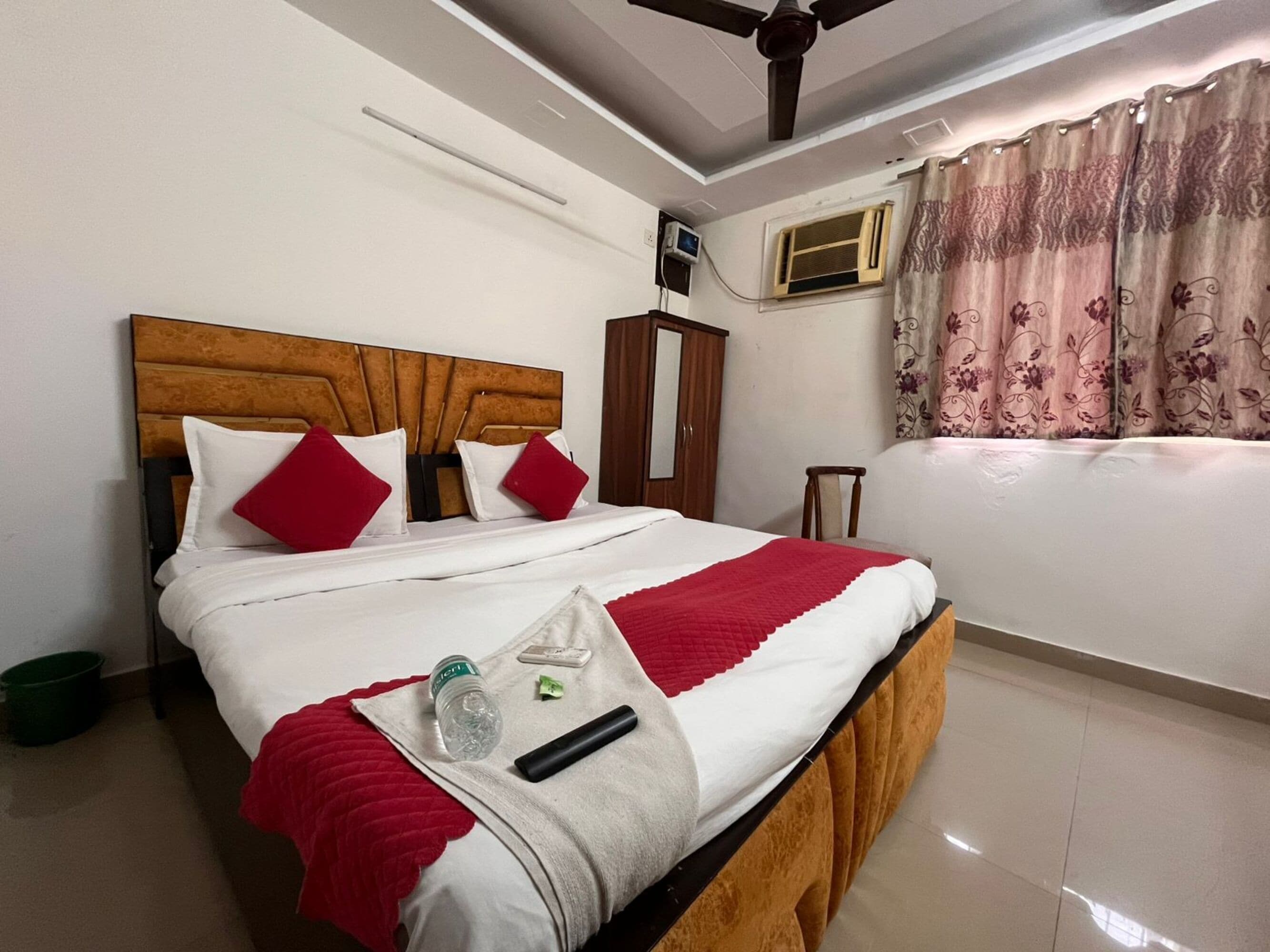 Habitación de hotel con cama, ventilador de techo, aire acondicionado y ventana con cortinas.