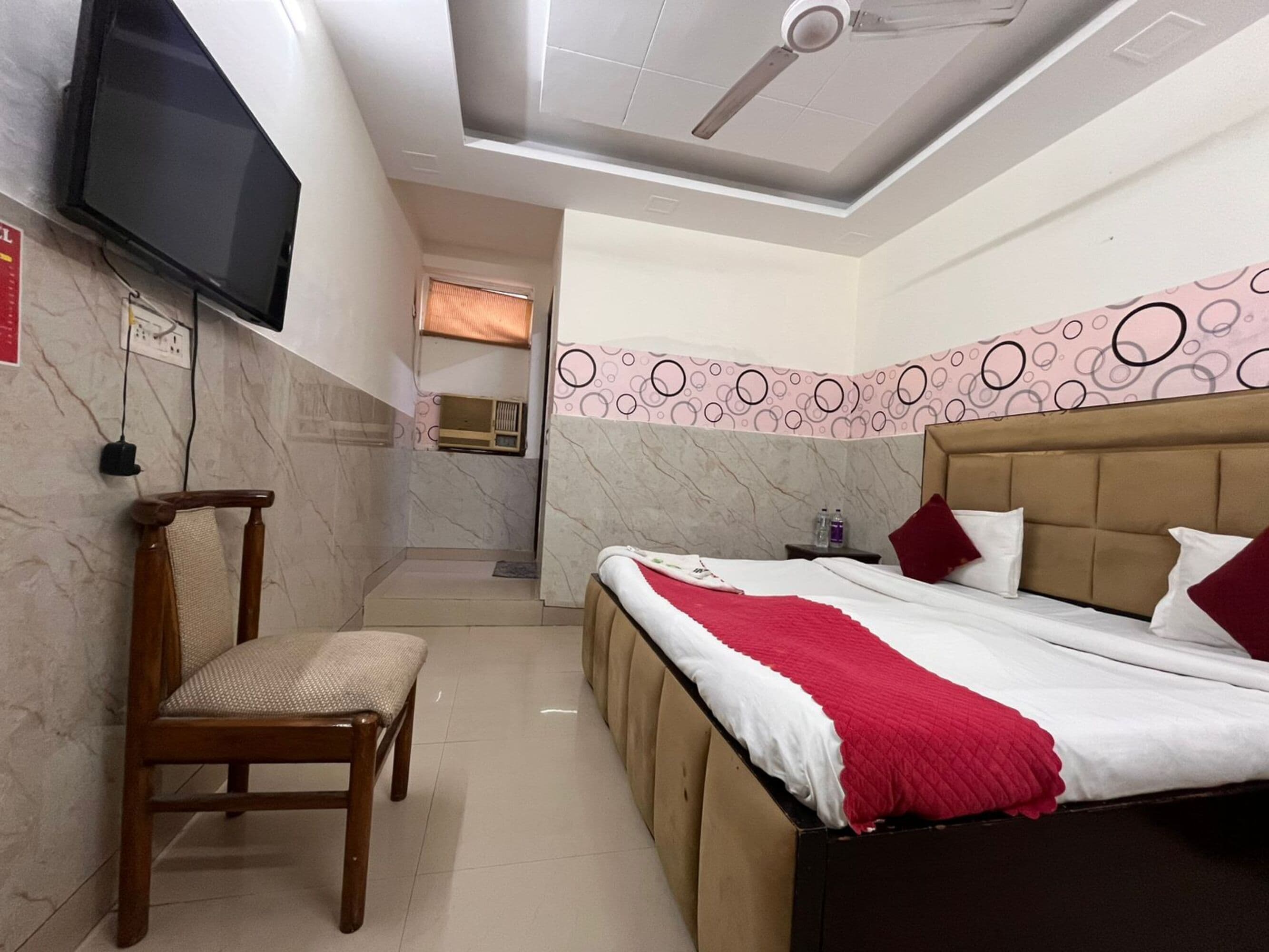 Una habitación de hotel con cama, una silla, un televisor y un ventilador de techo.