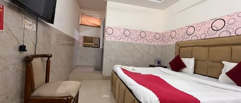 Una habitación de hotel con cama, una silla, un televisor y un ventilador de techo.
