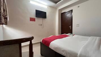 A hotel room with a bed, a desk, a chair, a television mounted on the wall, and a door.