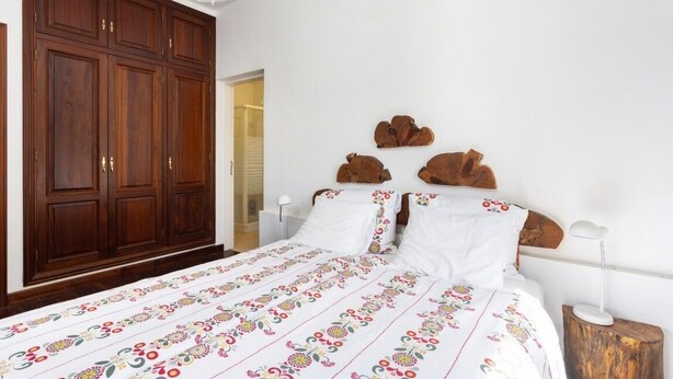 A bedroom with a large wooden wardrobe, a bed with floral bedding, and decorative wooden headboards. - FINCA LOS GERANIOS: A charming rural home on an incredible estate in Tegueste. (CN)