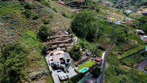 A residential area with a house featuring a swimming pool, surrounded by lush greenery and a winding road. - FINCA LOS GERANIOS: A charming rural home on an incredible estate in Tegueste. (CN)