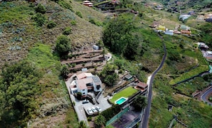 Ein Wohngebiet mit einem Haus, das einen Swimmingpool hat, umgeben von üppiger Vegetation und einer kurvenreichen Straße.