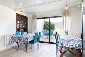 A dining area with a table set for four, blue chairs, a wooden cabinet, and a view through a glass door to the outside.
