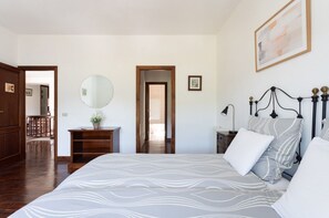 A bedroom with a large bed, a bedside table, a nightstand, a mirror, and a door leading to another room. - FINCA LOS GERANIOS: A charming rural home on an incredible estate in Tegueste. (CN)