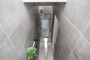 A narrow, tiled hallway with a central metal radiator, a small potted plant, and a vent at the end. - Bright 1BR Flat near London's West End (London)