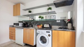 Uma cozinha compacta com armários de madeira, máquina de lavar embutida, micro-ondas e torradeira.