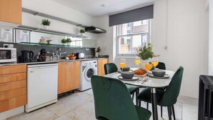 Cozinha moderna com lava-louças, máquina de lavar e área de refeições com mesa posta para dois.