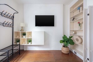 Een moderne woonkamer met een wandgemonteerde televisie, een bank, een plant en een kapstok aan de muur.