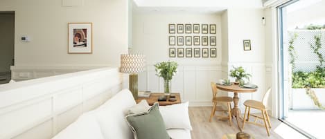 A modern living room with a sofa, a dining table with chairs, a lamp, and framed pictures on the wall.