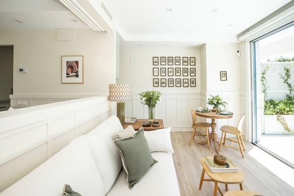 A modern living room with a sofa, a dining table with chairs, a lamp, and framed pictures on the wall.