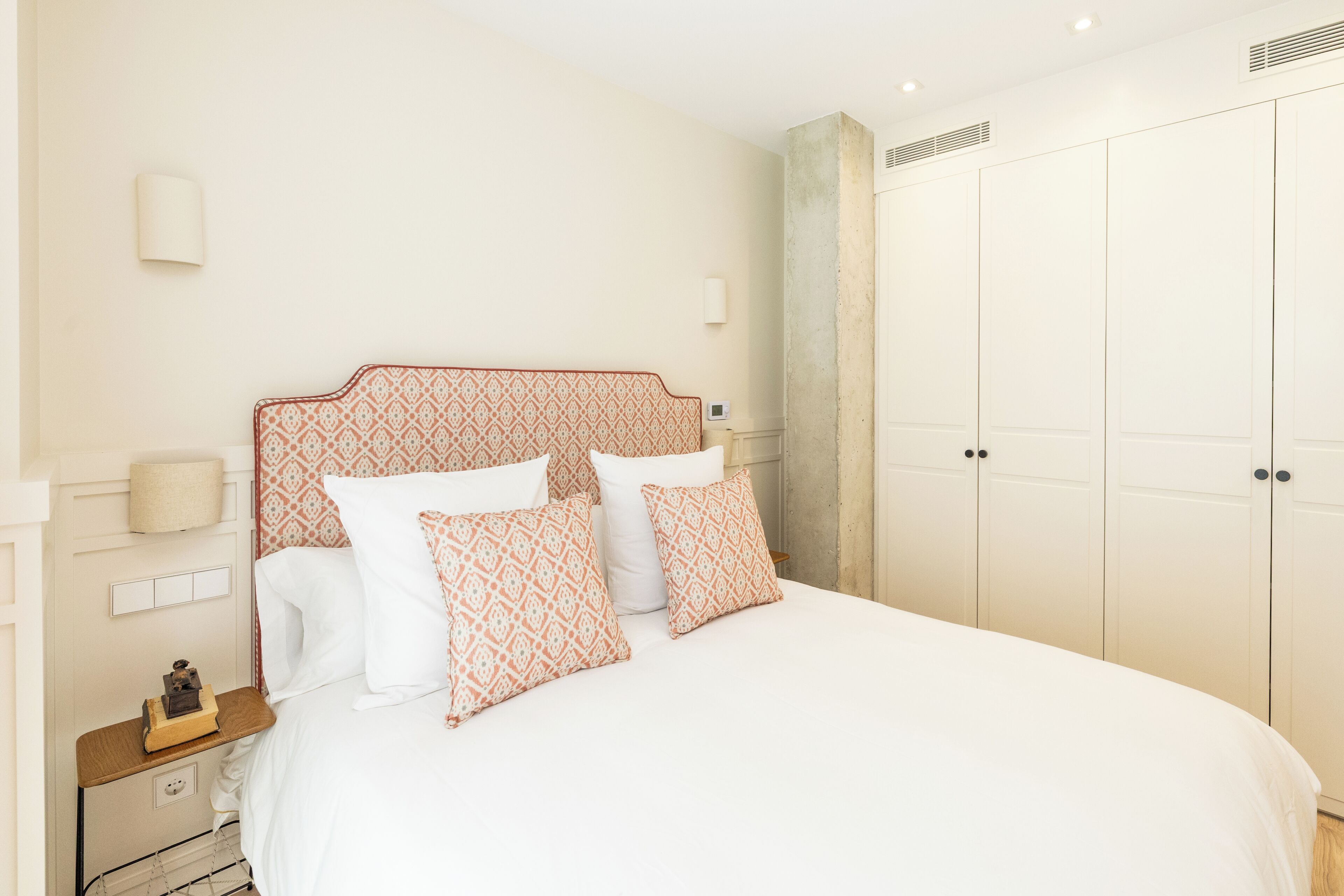 Quarto com uma cama grande, mesa de cabeceira, guarda-roupa e luminária na parede.