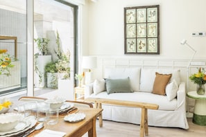 A modern living room with a white sofa, a wooden bench, and a dining table set with plates and glasses.