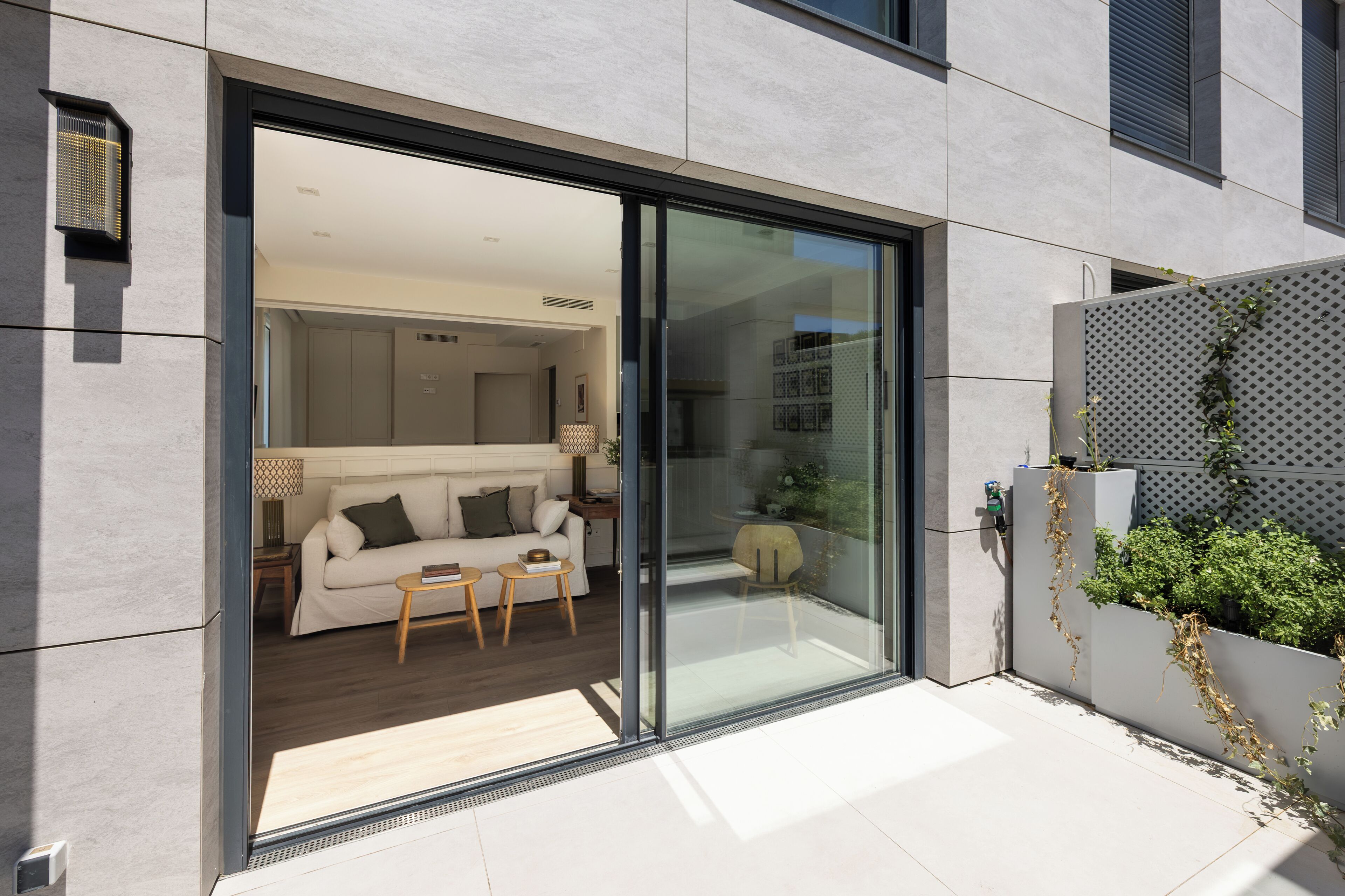 Een modern interieur met een bank, twee bijzettafels en een glazen deur naar een balkon.