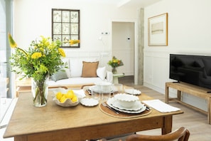 Un comedor con una mesa de madera lista para una comida, un jarrón con flores amarillas y un televisor sobre un mueble de madera.