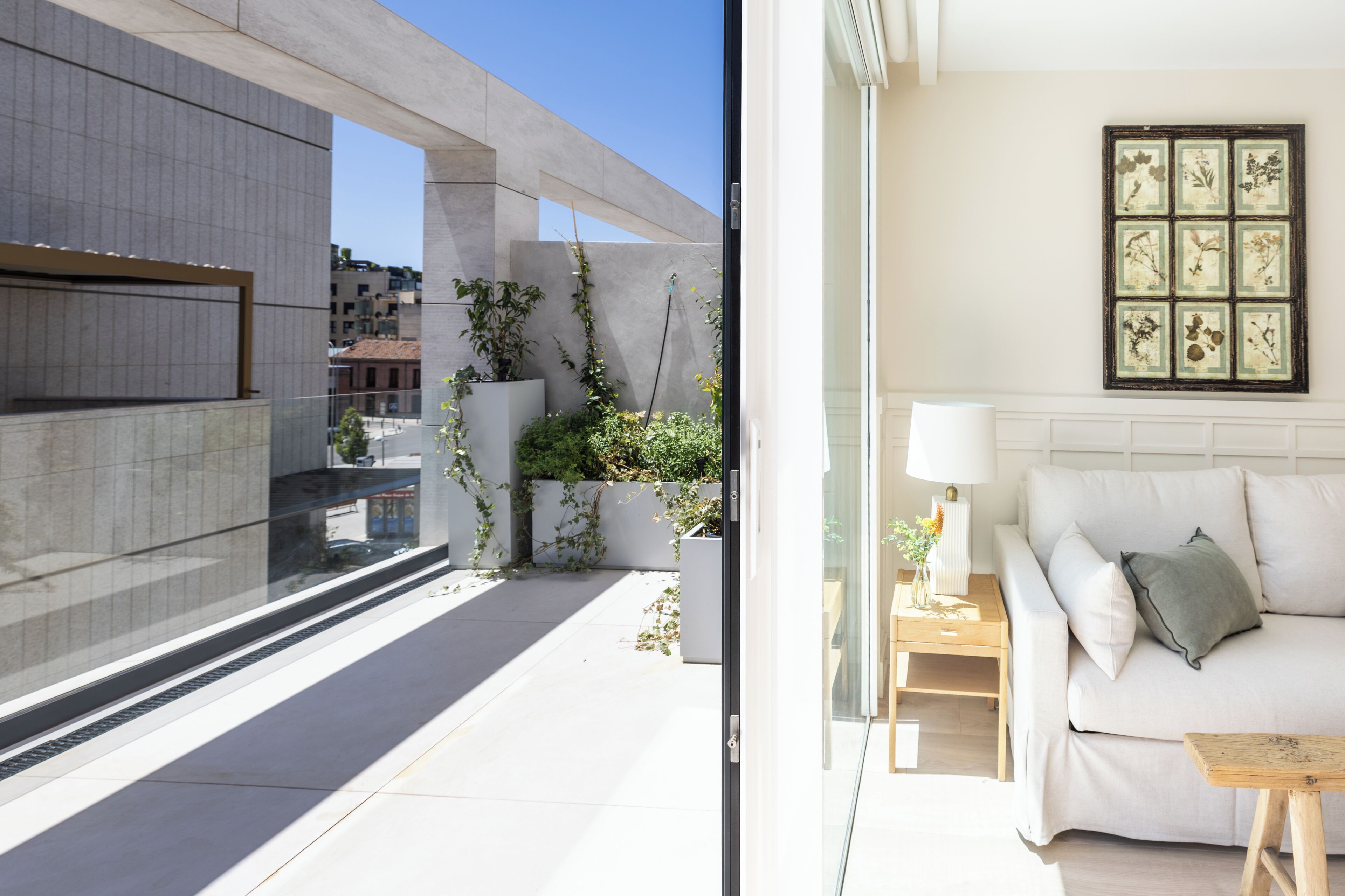 A modern living room with a white sofa, a small wooden side table, and a wall-mounted lamp.