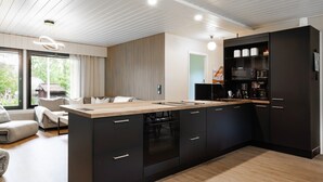 A modern kitchen with a central island, dark cabinetry, and a view of the outdoors. - Teddy`s Hideout, Private Sauna By Lapland Host (Rovaniemi)